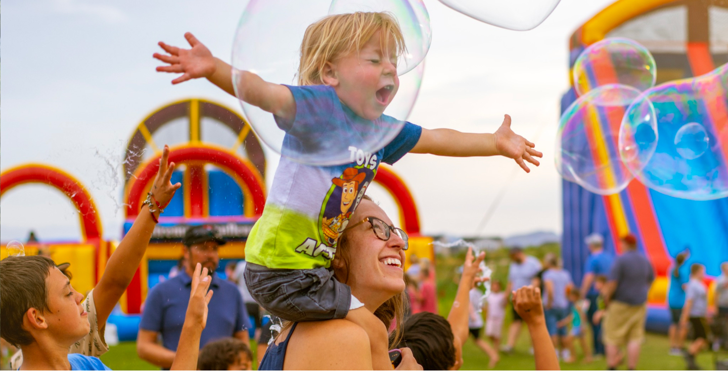 woman-smiling-at-kid-on-shoulders-with-bubbles